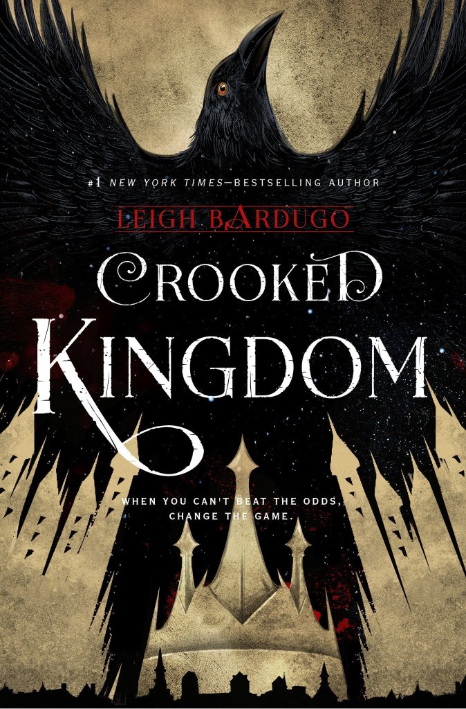 A book cover. The background is a dirty gold. A large image of a black crow with outstretched wings stretches across the entire cover. Its tail feather are parted to look like a crown. Below it, at the bottom of the cover, the shadow of a small cityscape. Text in the centre reads:
"#1 New York Times- Bestselling Author" in small white capitals.
The author's name "Leigh Bardugo" directly below this, in larger red capitals. 
The title of the book "Crooked Kingdom" in even large white capitals. 
The tag line "When you can't beat the odds, change the game." in small white capitals. /end